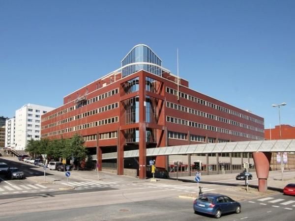 Moderni punaruskea toimistorakennus ja ylikulkusilta kaupunkiympäristössä.