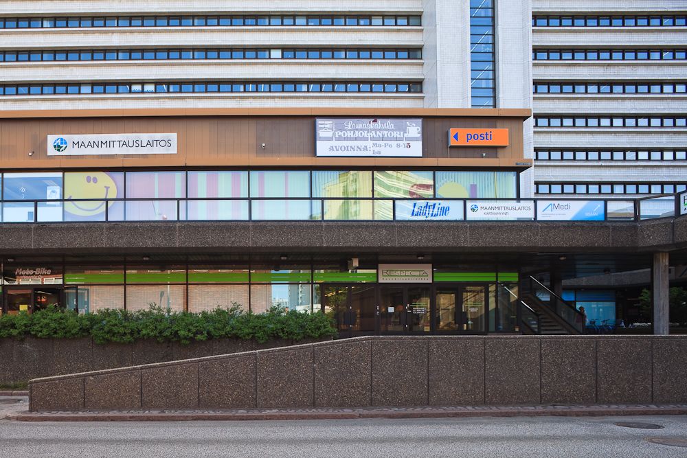 Monikerroksinen rakennus, jonka julkisivussa on useita liiketilojen ja virastojen kylttejä, kuten...