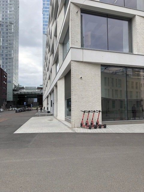 Neljä punaista sähköpotkulautaa pysäköitynä modernin rakennuksen viereen kaupunkiympäristössä.
