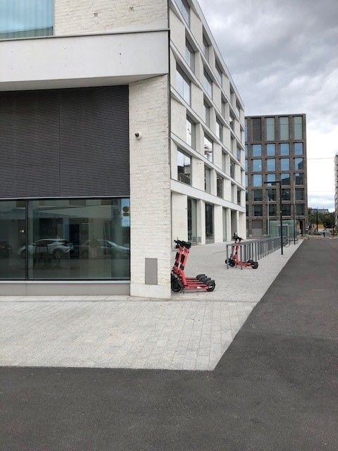 Punaisia sähköpotkulautoja pysäköitynä modernin valkoisen rakennuksen eteen kaupunkiympäristössä.