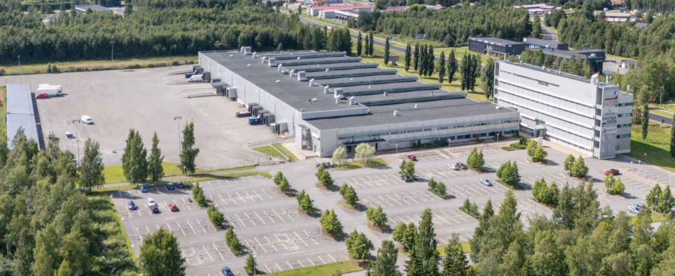 Ilmakuva suuresta teollisuus- ja toimistorakennuskompleksista sekä sen laajasta pysäköintialueesta.
