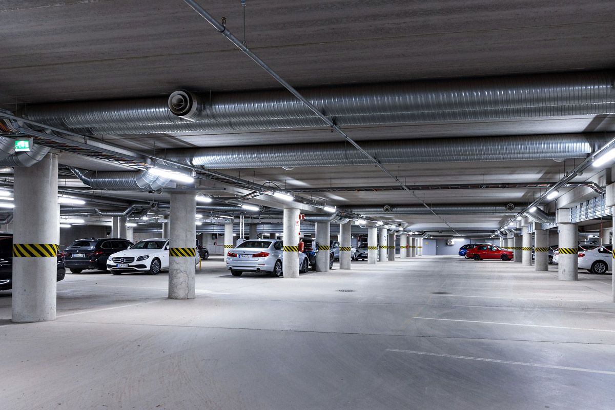 Valoisa pysäköintihalli, jossa on useita pysäköityjä autoja ja betonisia tukipilareita.