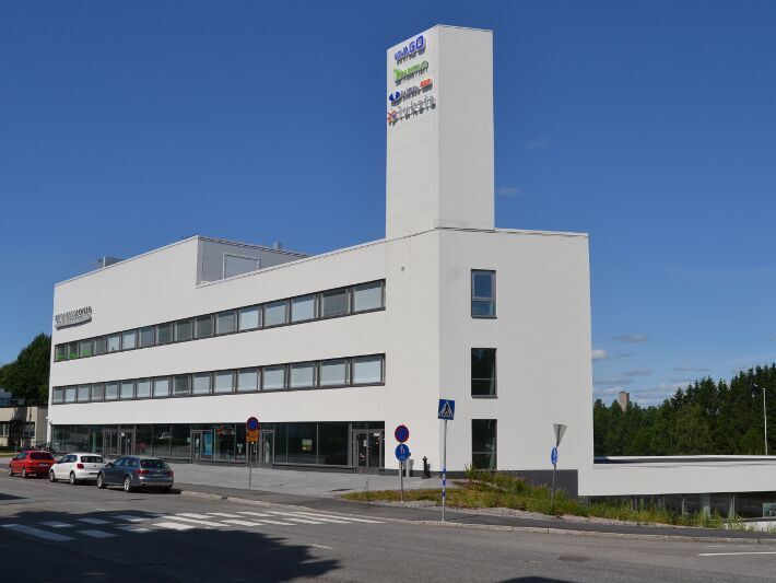 Valkoinen moderni toimistorakennus, jonka edessä on katu ja pysäköityjä autoja.