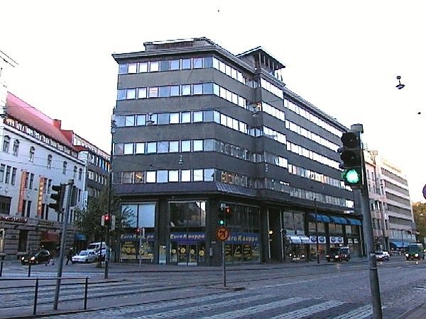 Kaupunkinäkymä, jossa on suuri harmaa rakennus kadun kulmassa.