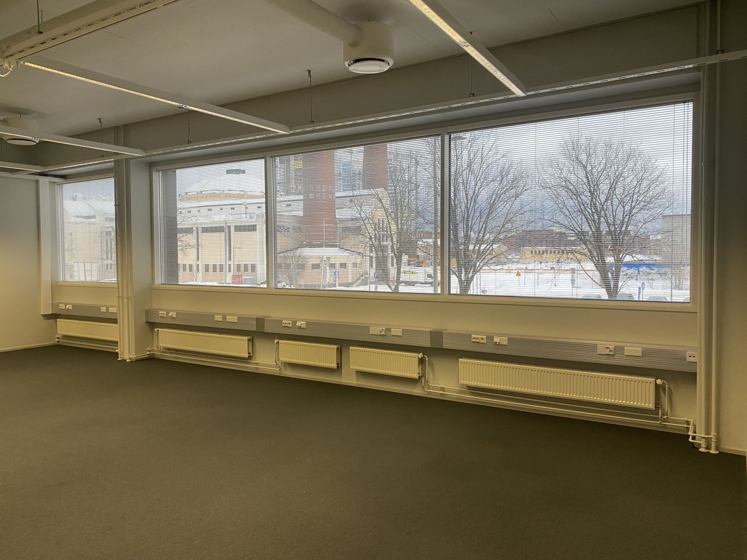 Tyhjä valoisa toimistotila, jossa on suuret ikkunat ja näkymä ulos.