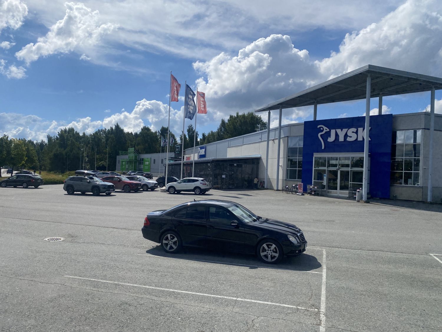 Musta auto pysäköitynä JYSK-myymälän edustalla olevalla suurella parkkipaikalla aurinkoisena päiv...