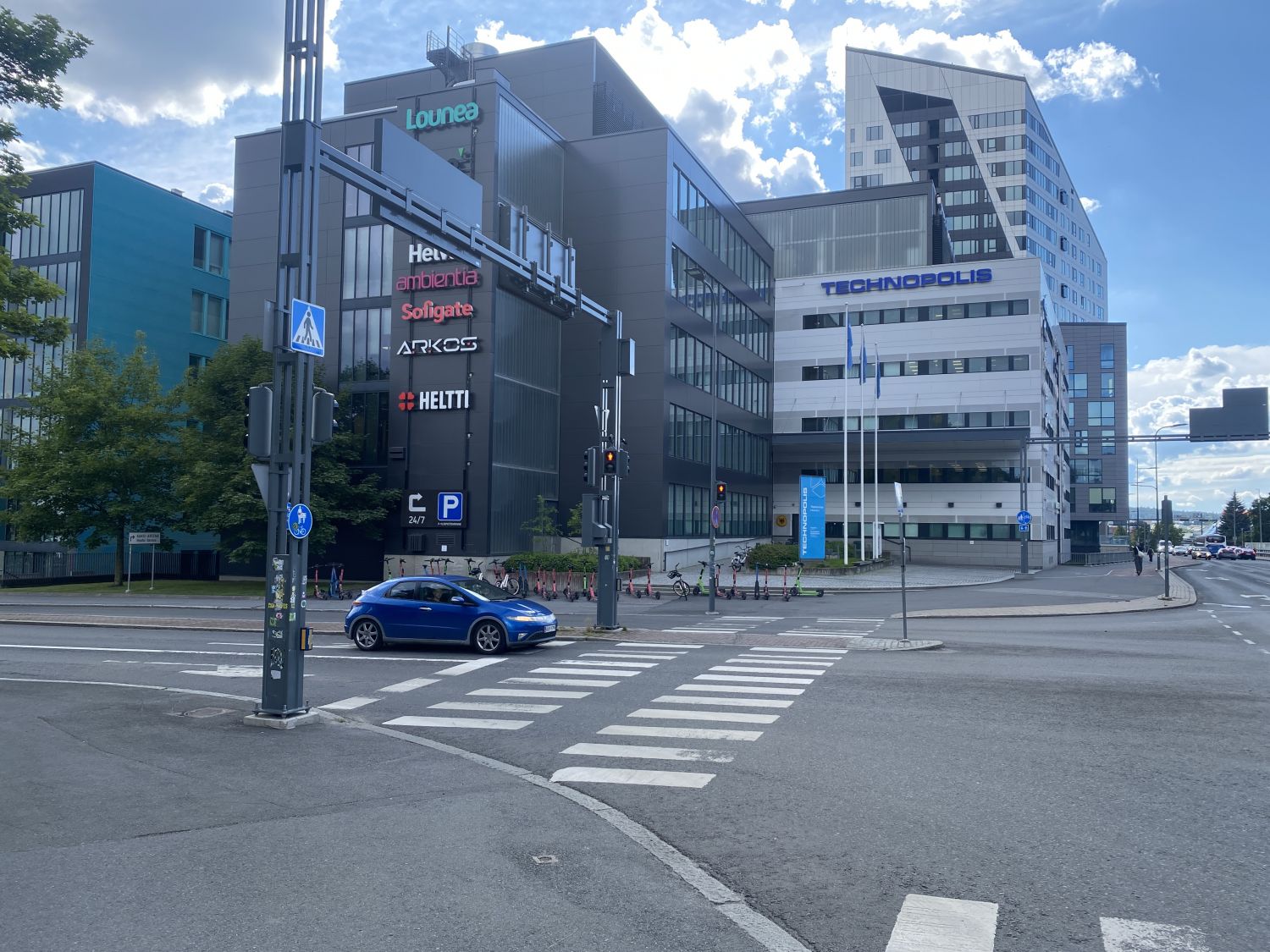 Näkymä kaupunkiristeyksestä, jossa on moderneja toimistorakennuksia ja suojatietä ylittävä sinine...