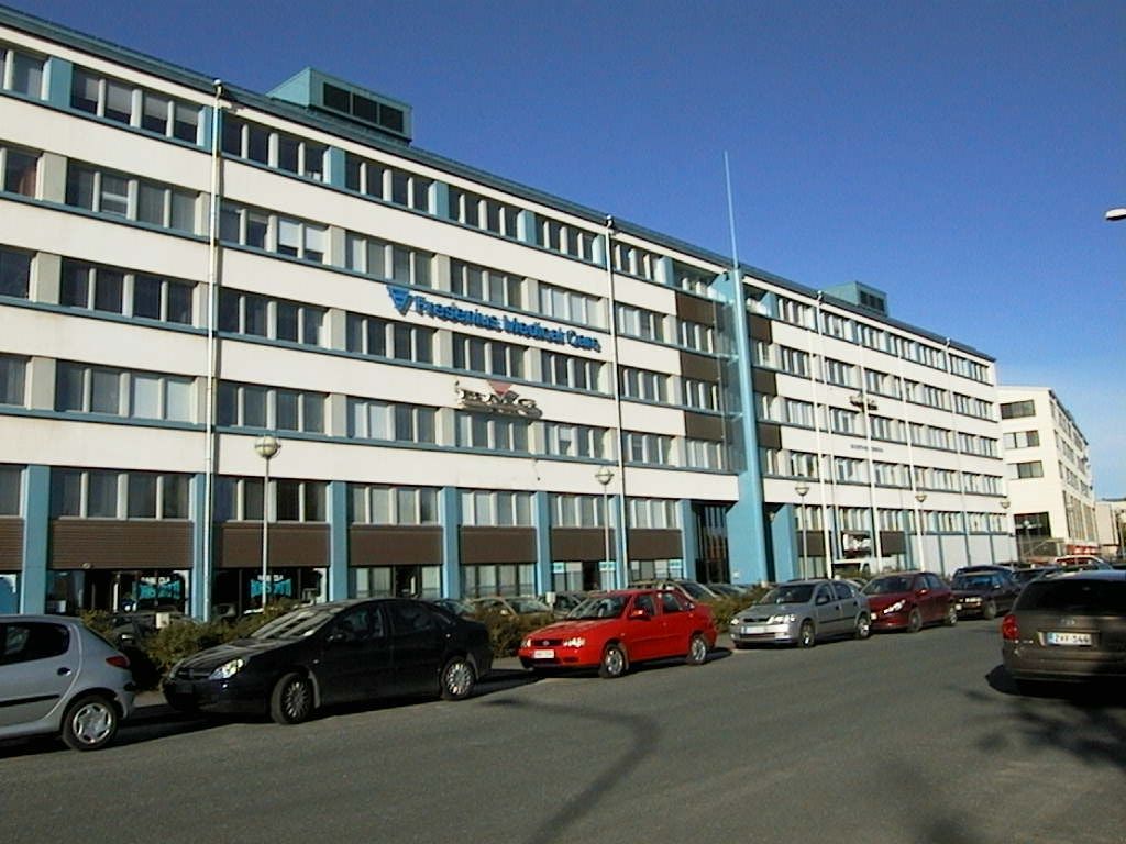 Valkoinen monikerroksinen toimistorakennus ja sen edustalle pysäköityjä autoja.