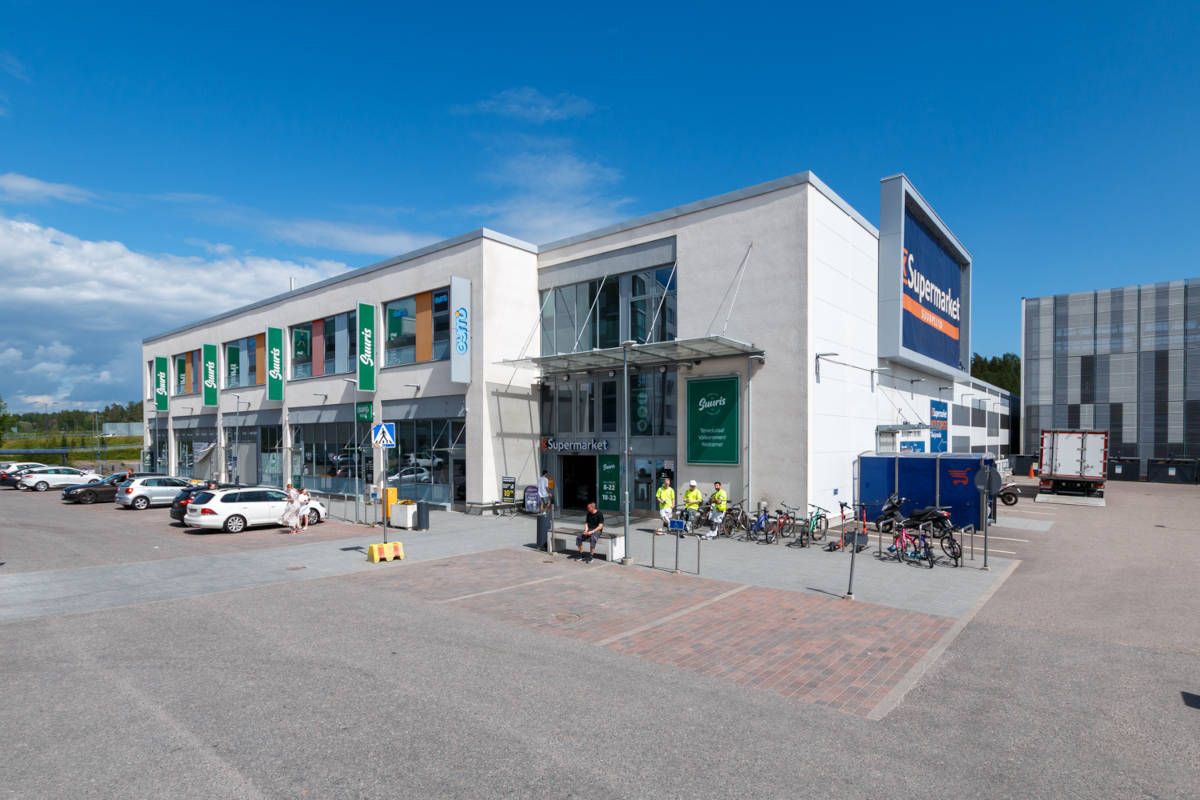 Moderni liikerakennus ja pysäköintialue aurinkoisena päivänä.