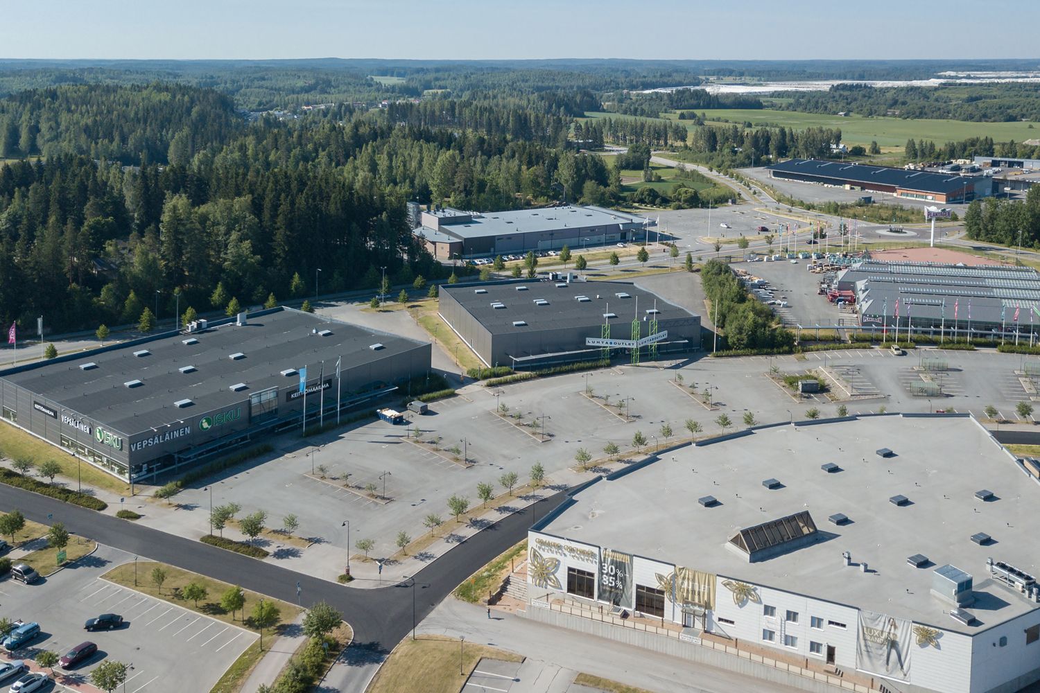 Ilmakuva liikealueesta, jossa on suuria myymälärakennuksia, laajoja pysäköintialueita ja ympäröiv...