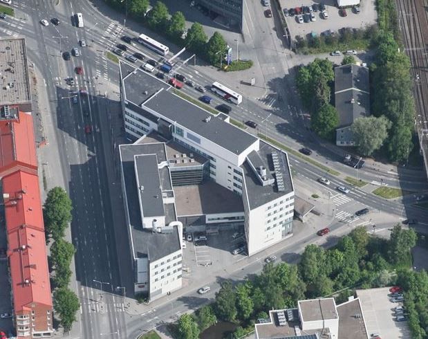 Ilmakuva kaupunkinäkymästä, jossa on moderni rakennuskompleksi, vilkkaita katuja ja puustoa.