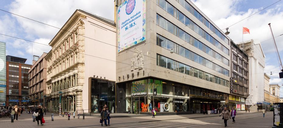 Kaupunkinäkymä Helsingin Aleksanterinkadulta, jossa on liikerakennuksia ja jalankulkijoita.