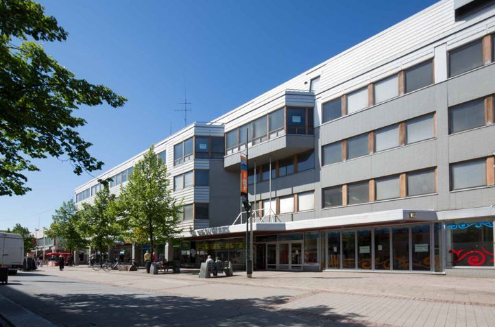 Monikerroksinen rakennus ja kävelykatu aurinkoisena päivänä.