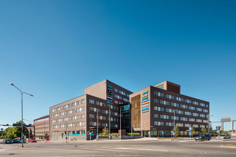 Moderni tumma toimistorakennus kadun risteyksessä aurinkoisena päivänä.