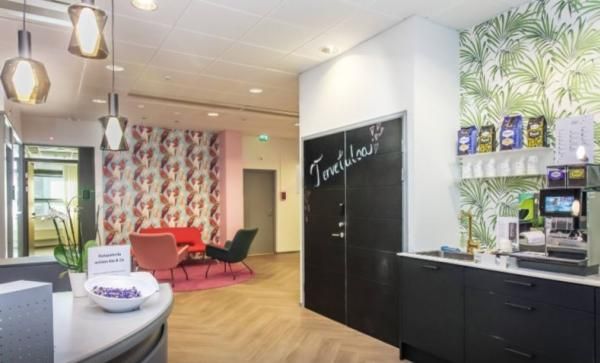 Värikäs ja valoisa toimiston aula, jossa on oleskelutila, vastaanottotiski ja kahvipiste.