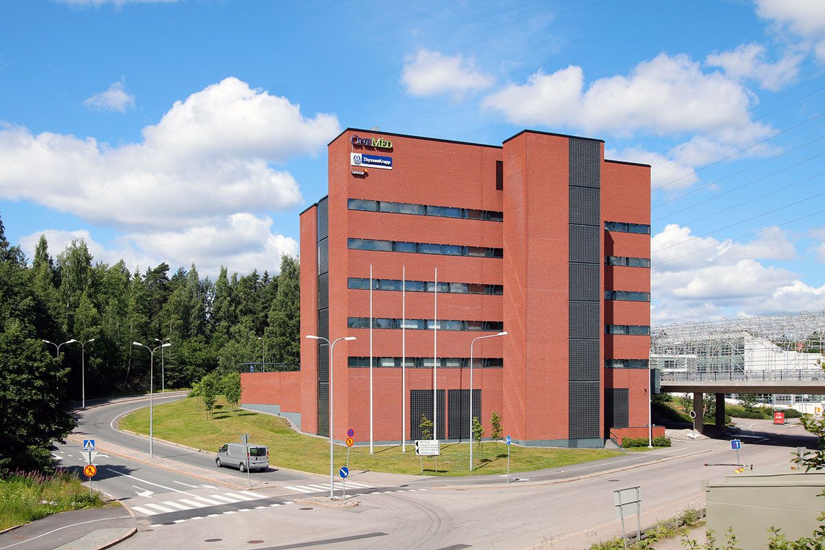 Nykyaikainen punatiilinen toimistorakennus ja katu aurinkoisena päivänä.