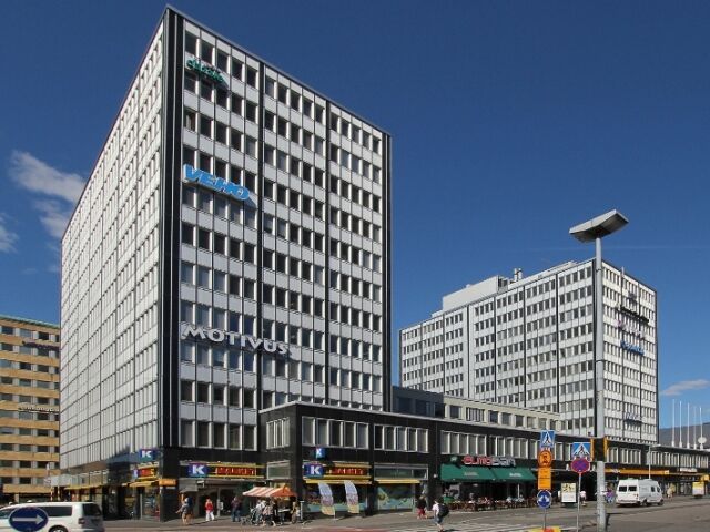 Kaksi korkeaa, modernia toimistorakennusta aurinkoisessa kaupunkimaisemassa.