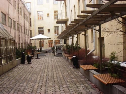 Kivetty sisäpiha rakennusten välissä, jossa on penkkejä ja puinen pergola.