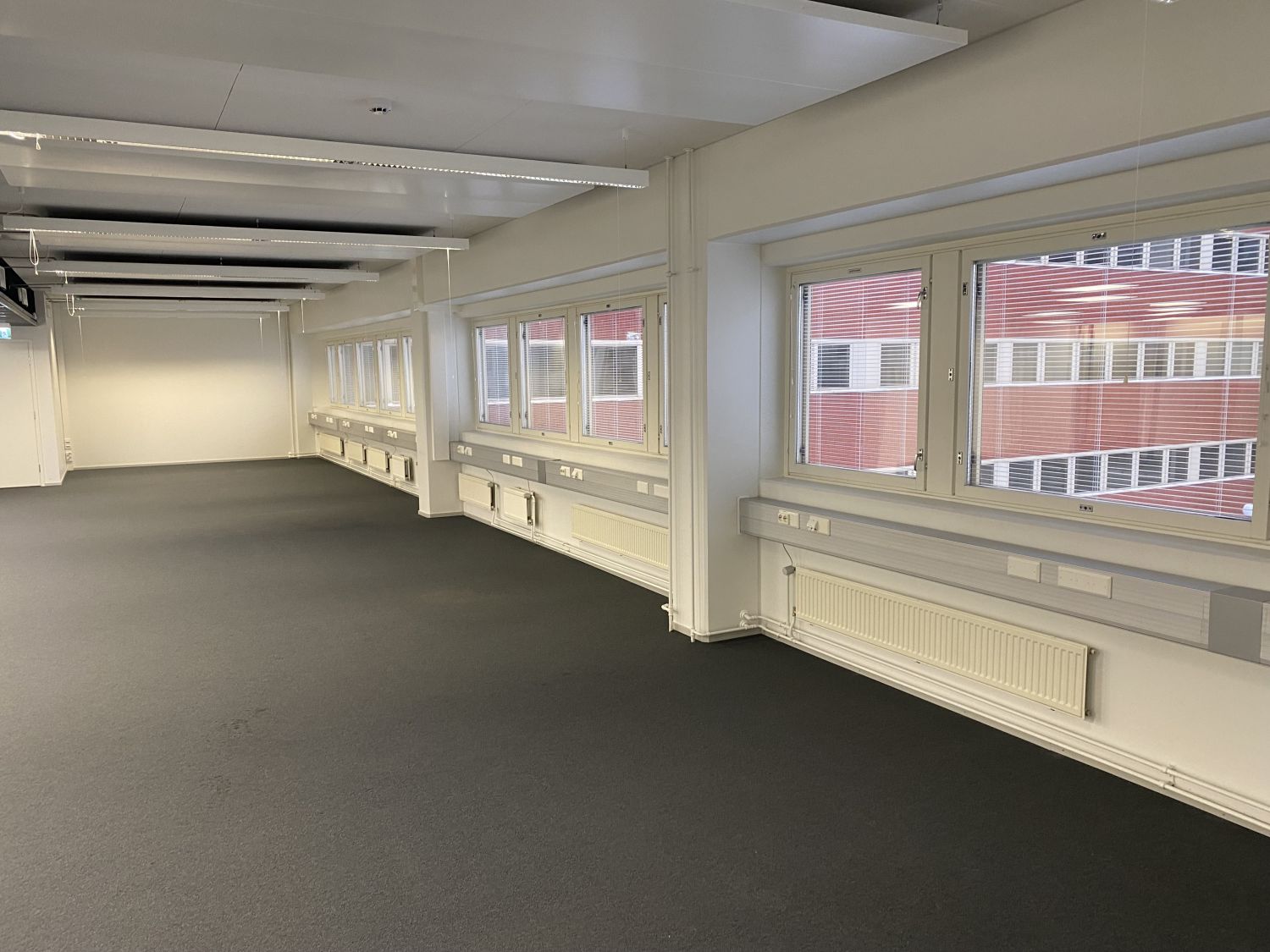 Tyhjä moderni toimistotila, jossa on harmaa matto ja suuret ikkunat.