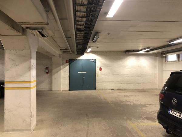 Näkymä sisäpysäköintihallista, jossa on etualalla betonipilari keltaisilla raidoilla, taustalla v...