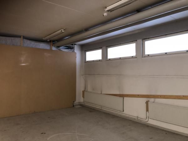 Tyhjä teollisuus- tai varastotila, jossa on betonilattia, vaaleat seinät, yläikkunoita ja kattopu...