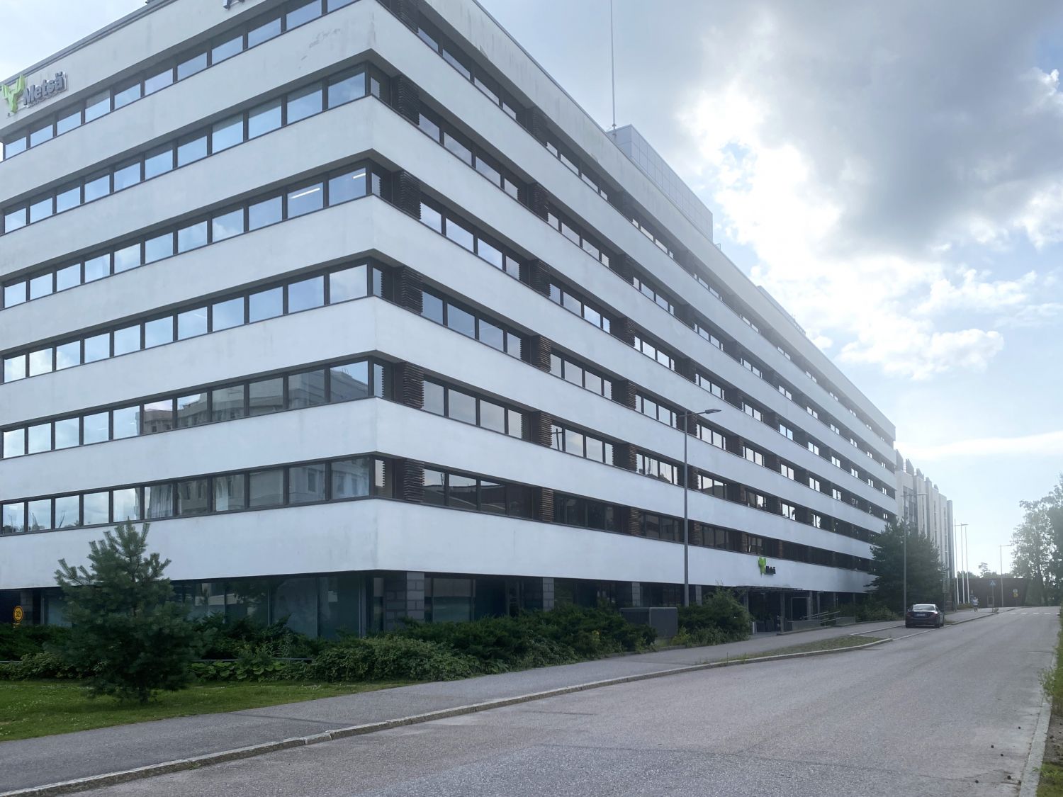 Valkoinen monikerroksinen toimistorakennus tien vieressä pilvisenä päivänä.