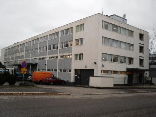 Monikerroksinen vaalea rakennus ja sen edessä olevia autoja.