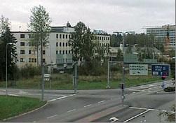 Näkymä kadunristeyksestä, jossa on opasteita ja taustalla rakennuksia.