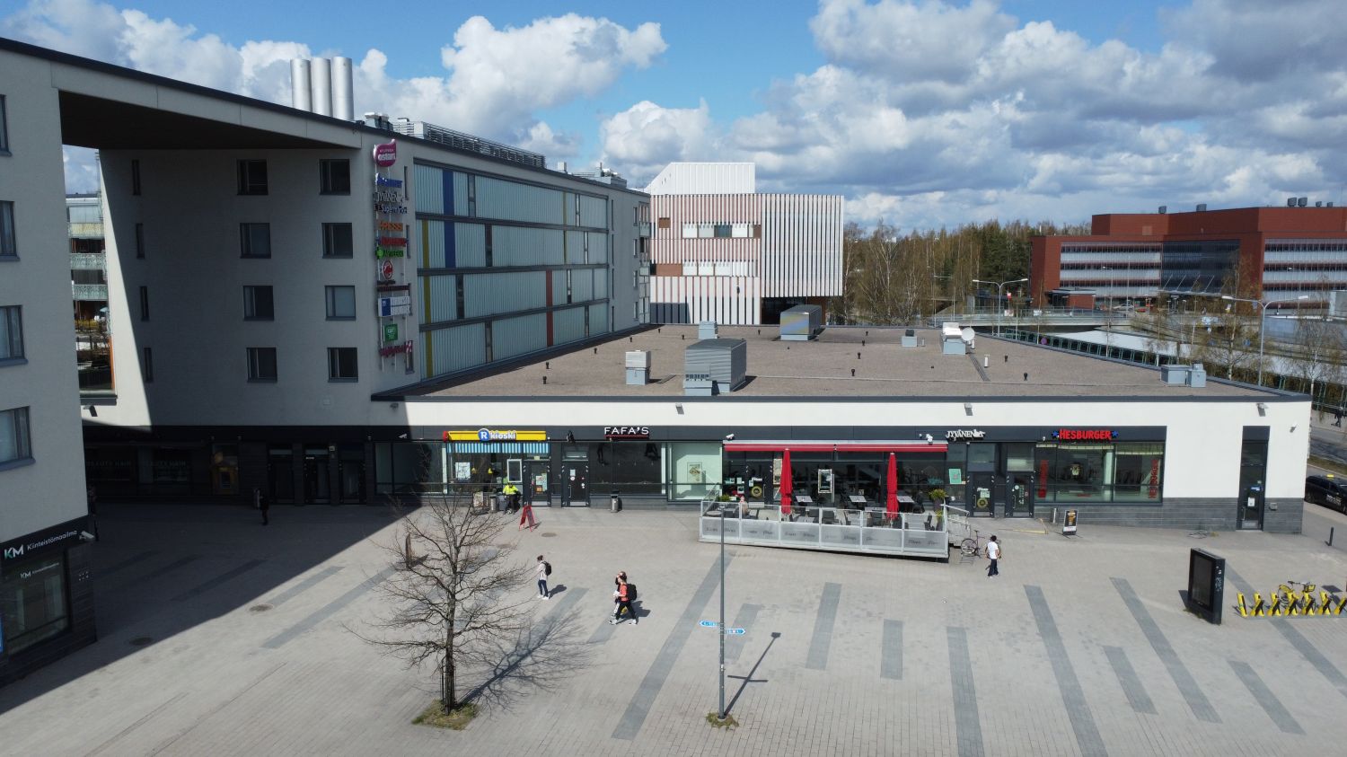 Korkealta otettu kuva modernista liikekeskuksesta ja sen edustalla olevasta kivetystä aukiosta, j...