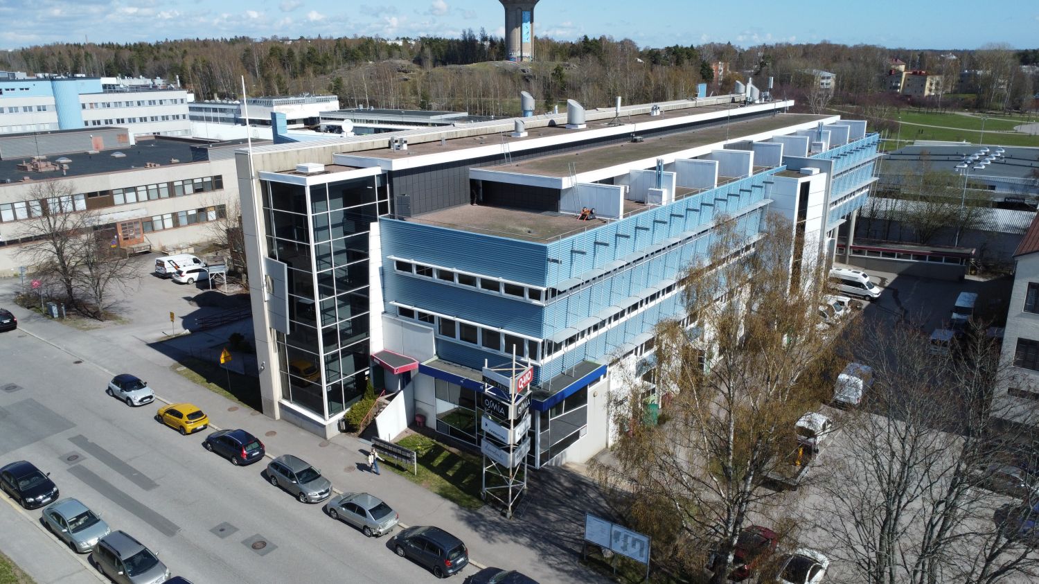 Ilmakuva modernista liikerakennuksesta ja sen edustalla olevasta kadusta autoineen.