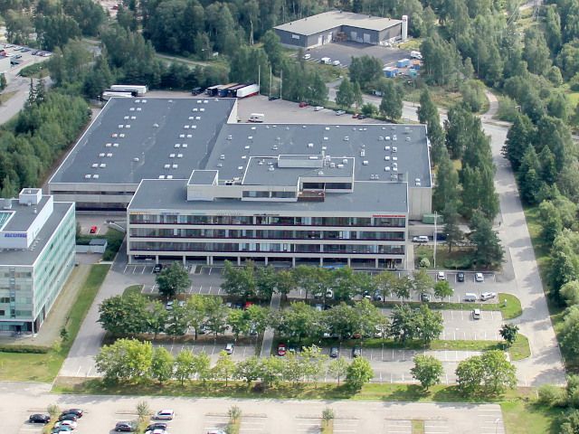 Ilmakuva toimisto- ja varastorakennuksista sekä niiden edessä olevasta laajasta parkkipaikasta.