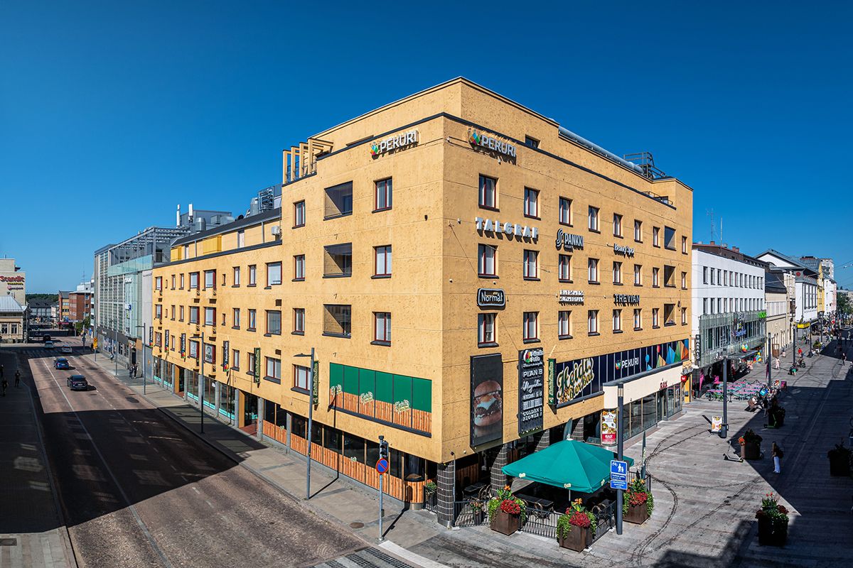 Keltainen liikerakennus kadun kulmassa kaupunkiympäristössä.
