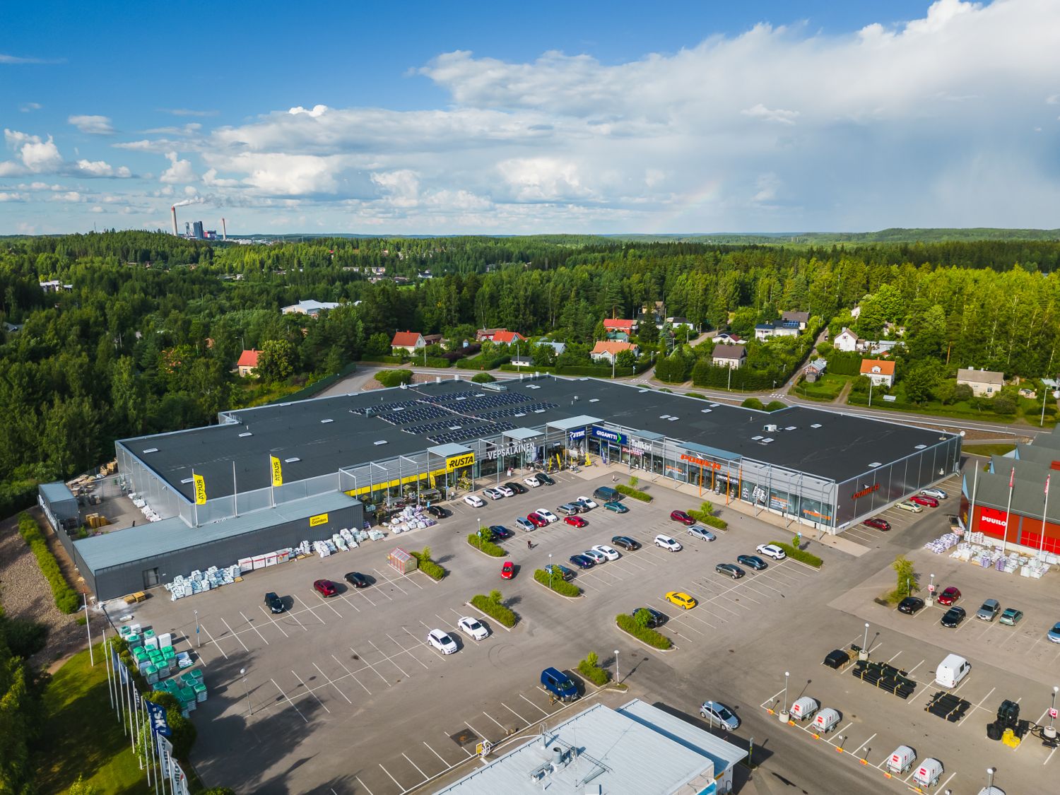 Ilmakuva liikekeskuksesta ja sen pysäköintialueesta metsäisessä maisemassa.