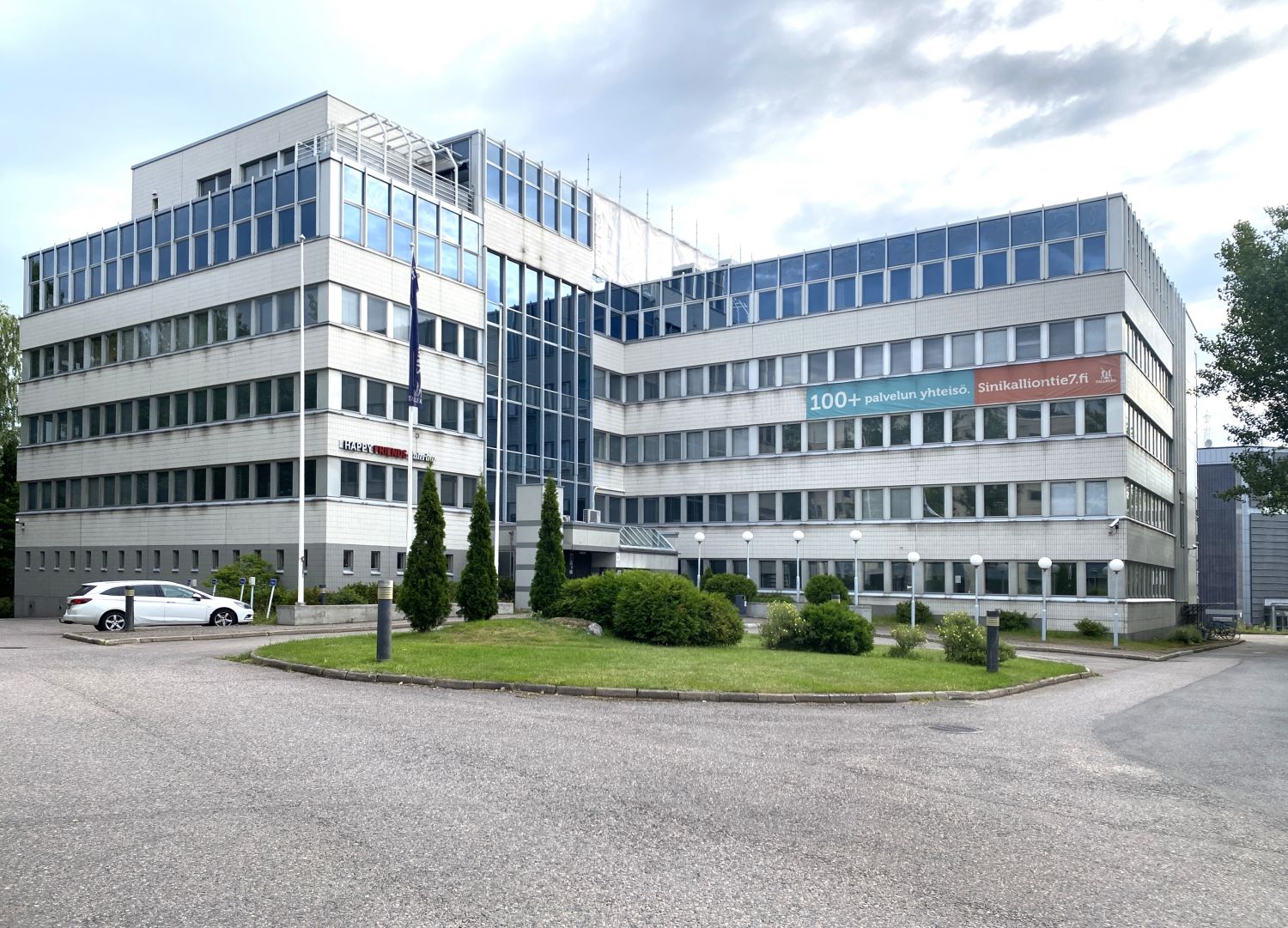 Vaalea monikerroksinen toimistorakennus ja sen edustalla oleva piha-alue.