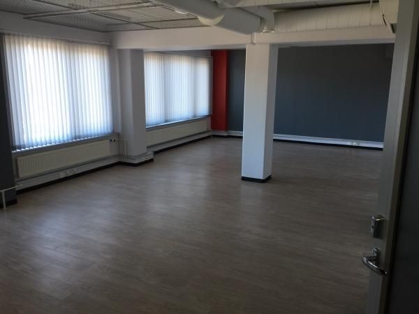 Tyhjä ja valoisa toimistotila, jossa on vaalea lattia ja suuret ikkunat.