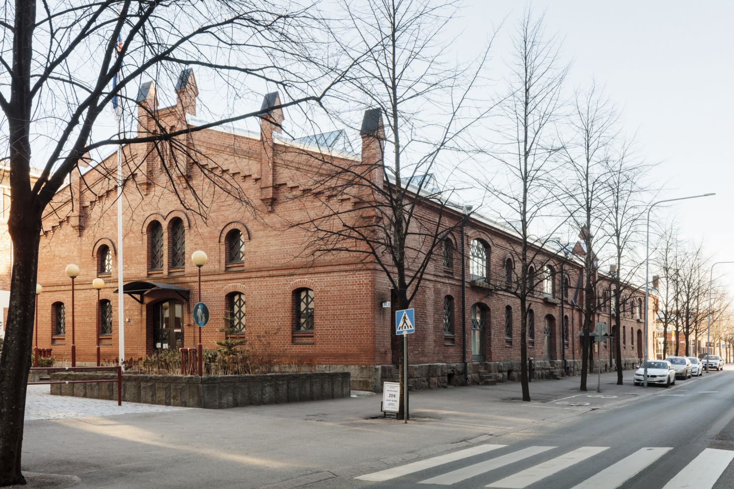 Punatiilinen rakennus kadun varrella paljaiden puiden takana.