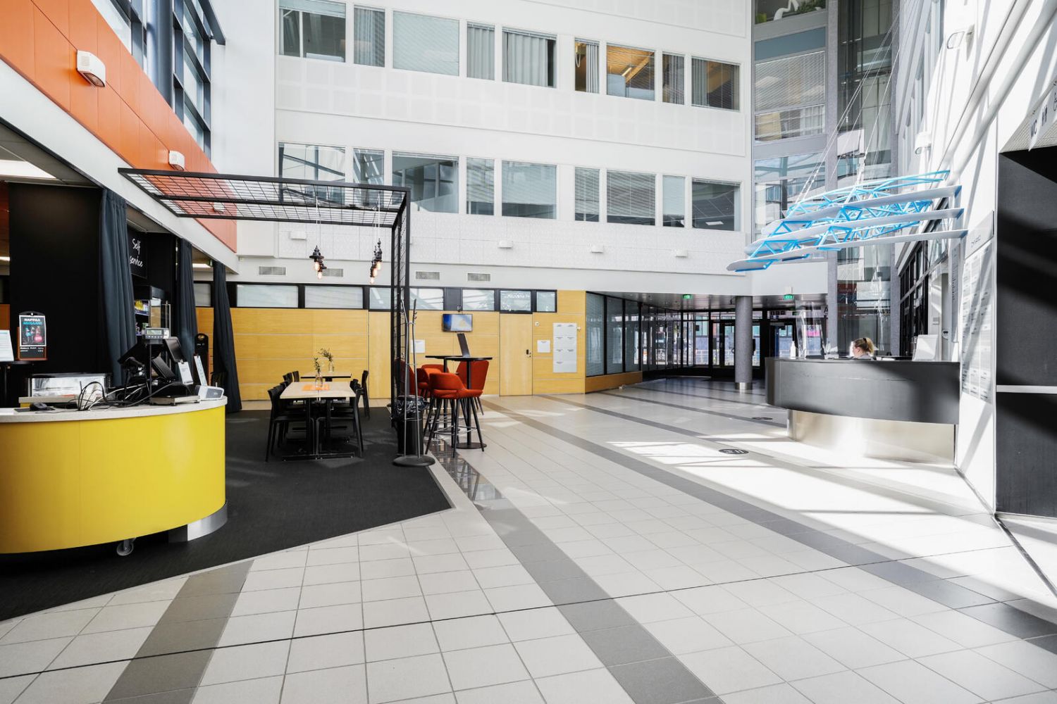 Valoisa ja moderni rakennuksen aula, jossa on palvelupisteitä ja istumaryhmiä.