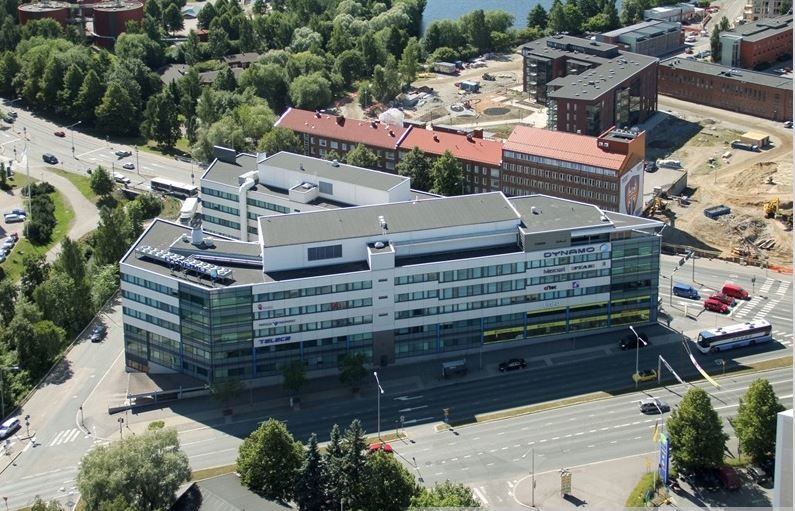 Ilmakuva modernista toimistorakennuksesta ja sitä ympäröivästä kaupunkiympäristöstä.