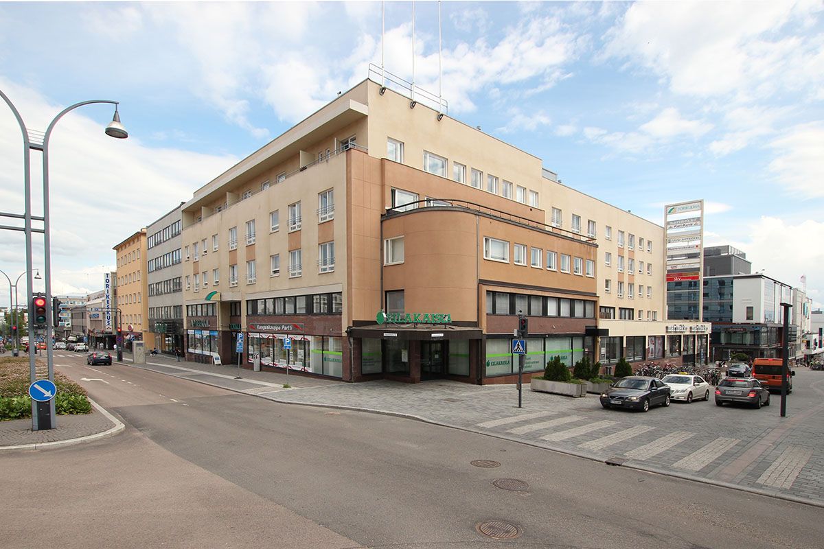 Monikerroksinen rakennus kaupungin kadun kulmassa ja katunäkymä, jossa on autoja.