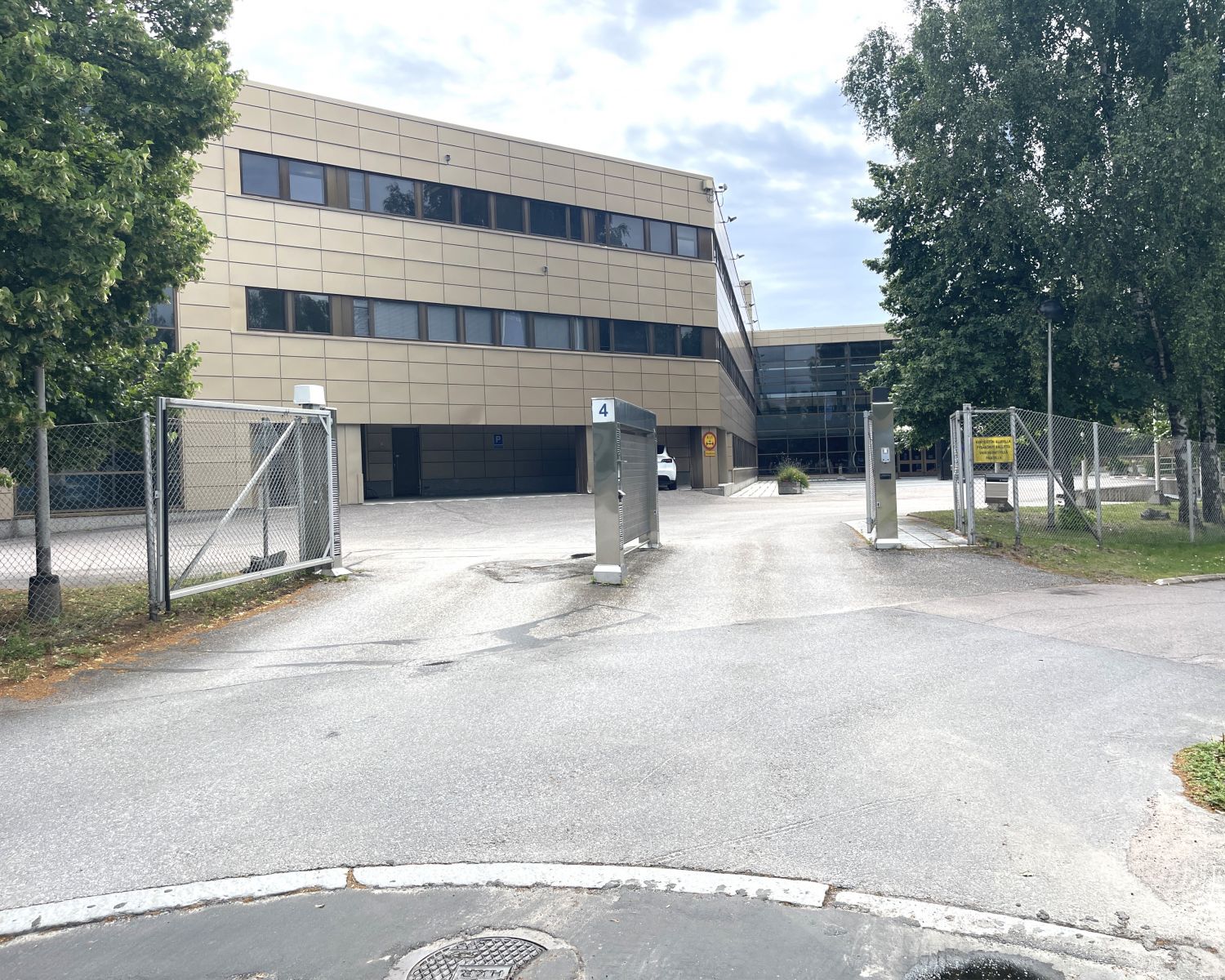 Näkymä portilta vaaleaan monikerroksiseen rakennukseen, jota ympäröivät puut.