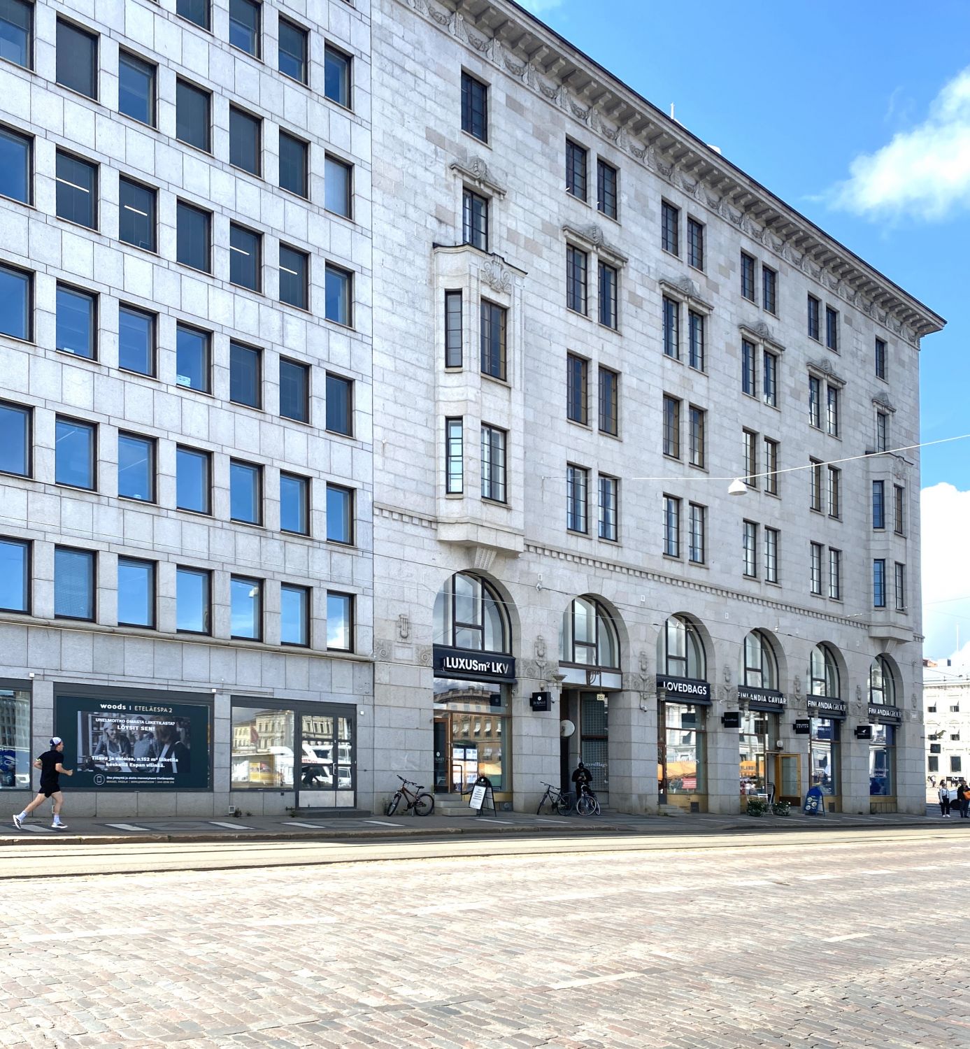 Suuri kivirakennus liiketiloineen ja sen edustalla oleva mukulakivikatu kaupungin keskustassa.