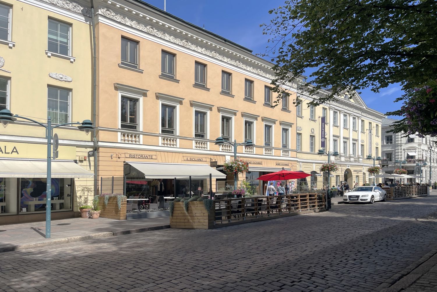 Aurinkoinen katunäkymä historiallisella mukulakivikadulla, jonka varrella on vanhoja rakennuksia ...