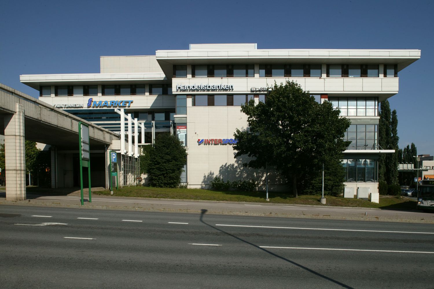 Valkoinen liikerakennus, jossa on Handelsbankenin, S-marketin ja Intersportin kyltit, monikaistai...
