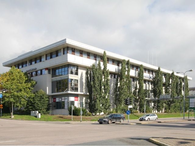 Valkoinen monikerroksinen toimistorakennus kadun kulmassa.