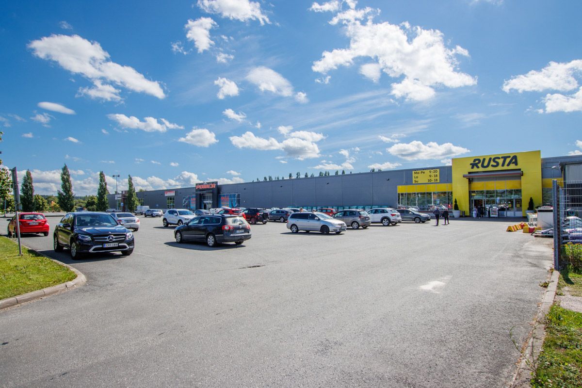 Liikekeskuksen parkkipaikka Rusta- ja Power-myymälöiden edustalla aurinkoisena päivänä.
