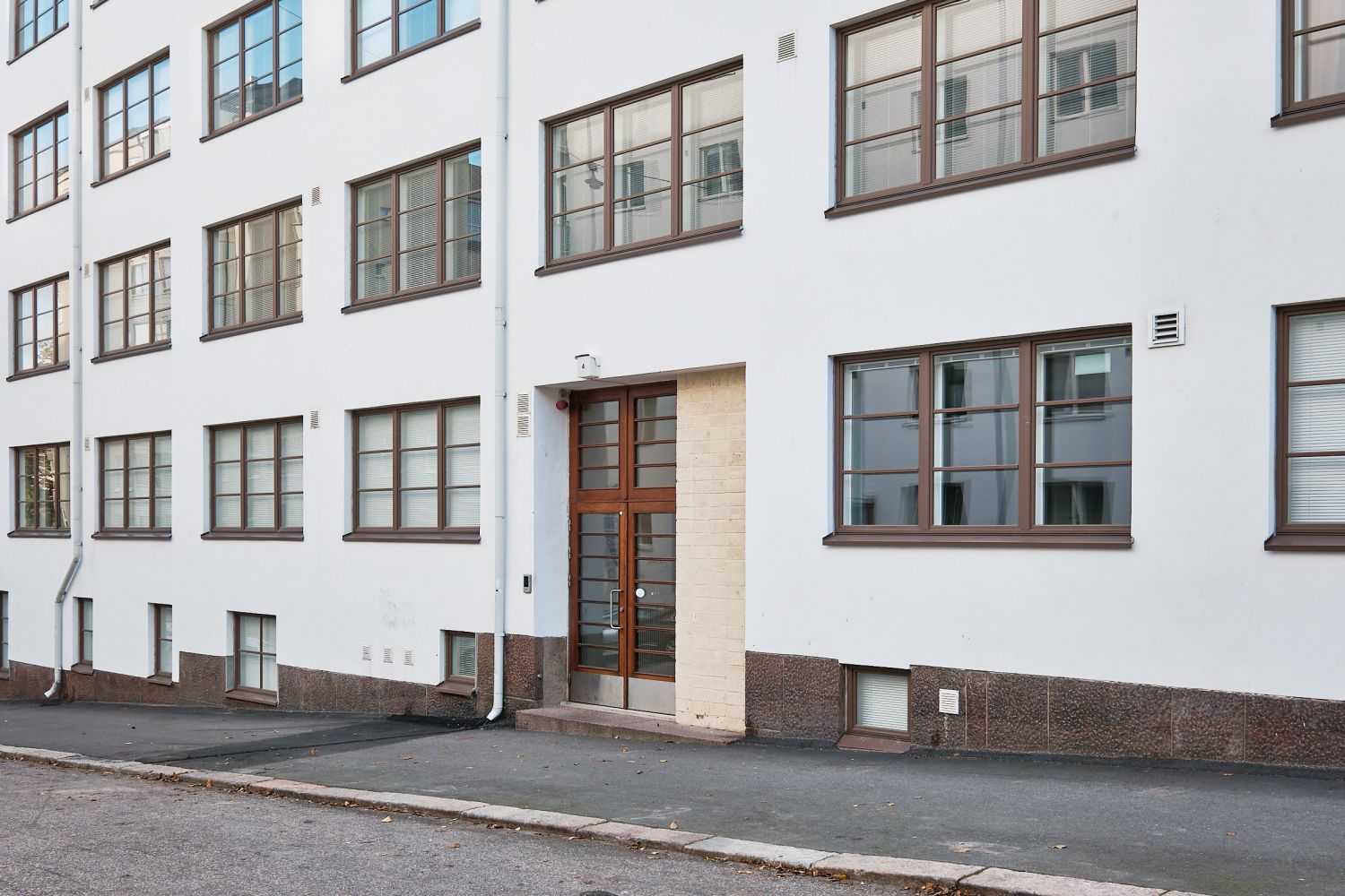 Valkoinen asuinkerrostalo, jossa on ruskeat ikkunat ja sisäänkäynti kadun varrella.