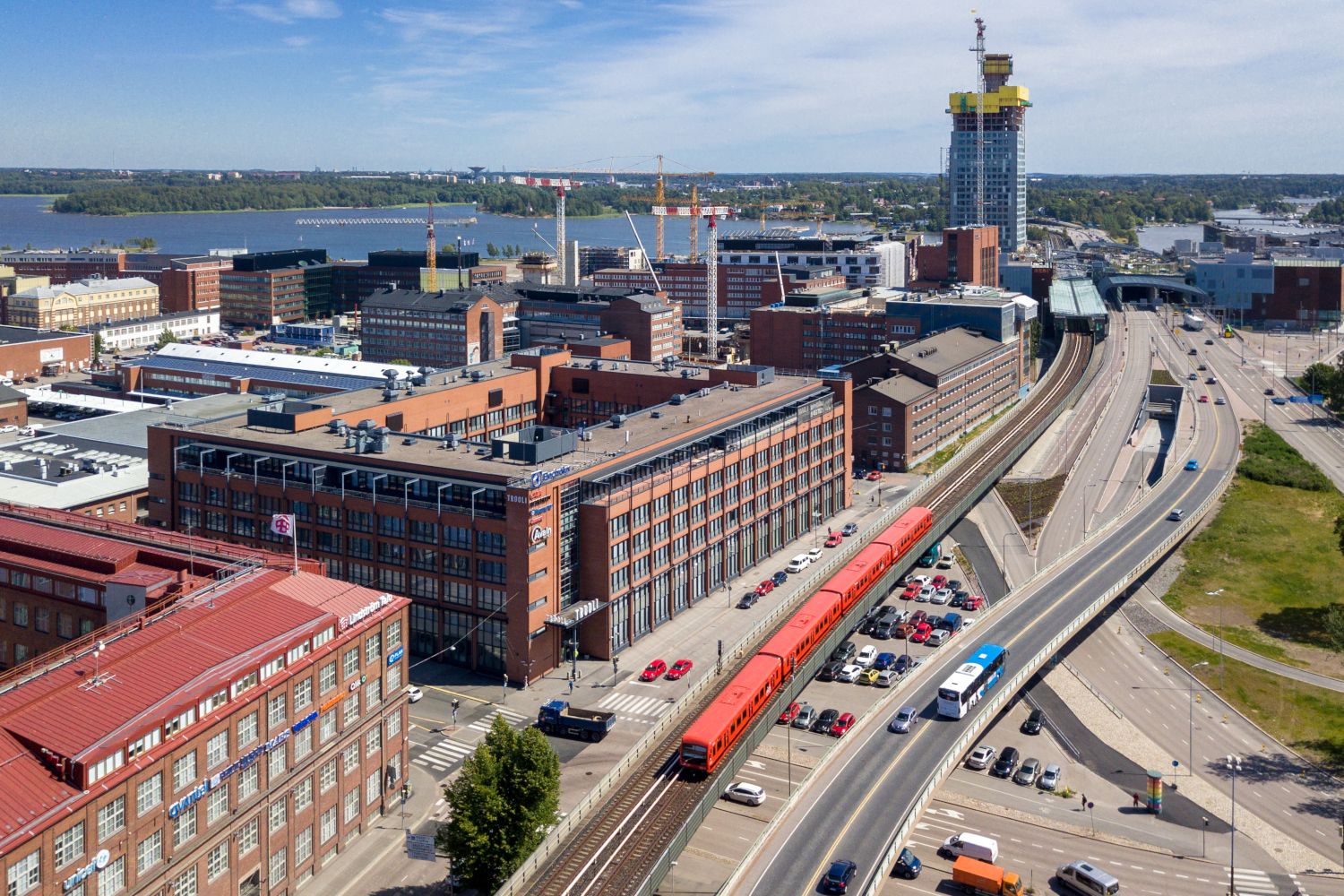 Korkealta otettu kaupunkikuva, jossa punainen metrojuna kulkee tiilirakennusten ja teiden välissä.