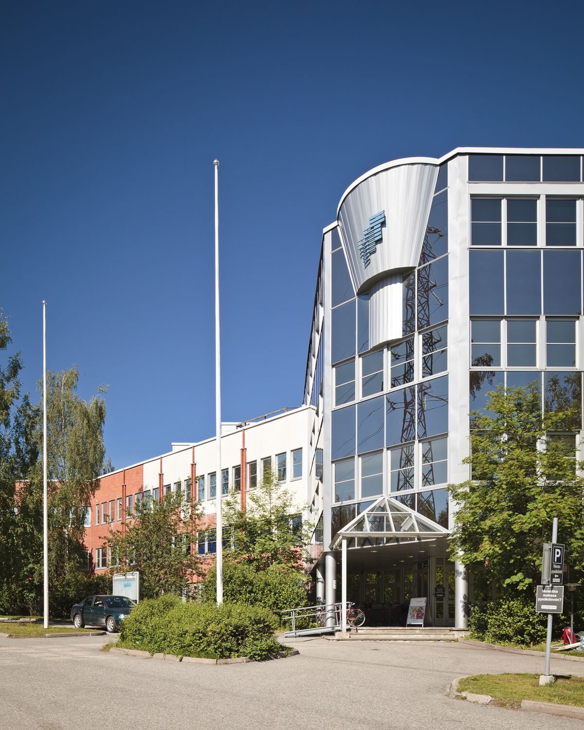 Moderni toimistorakennus, jonka edustalla on lipputankoja ja vehreitä istutuksia.