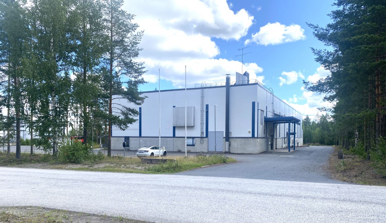 Moderni valkoinen teollisuusrakennus metsäisessä ympäristössä aurinkoisena päivänä.