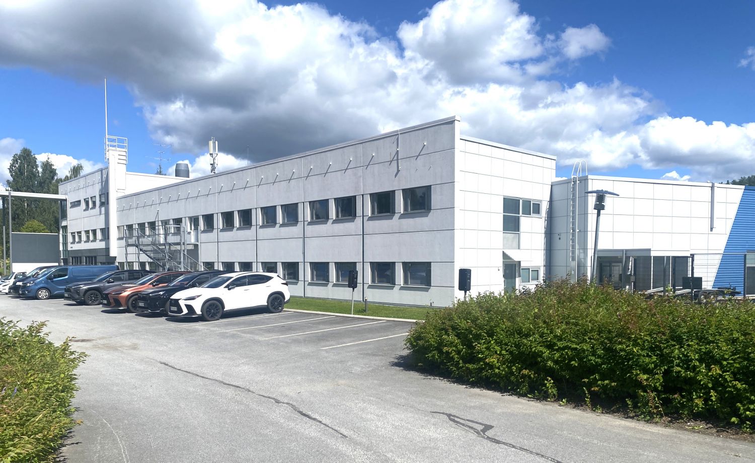 Valkoinen toimistorakennus ja parkkipaikalla olevat autot aurinkoisena päivänä.